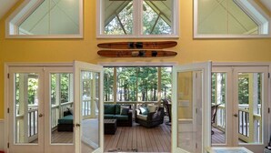 A covered deck with a sofa and chairs, a wooden boat, and a view of trees. - Water You Wating For? | Waterfront Fun & Relaxation (Boydton)