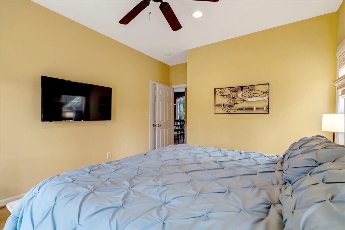 A bedroom with a bed, a ceiling fan, a mounted TV, and a door leading to another room.