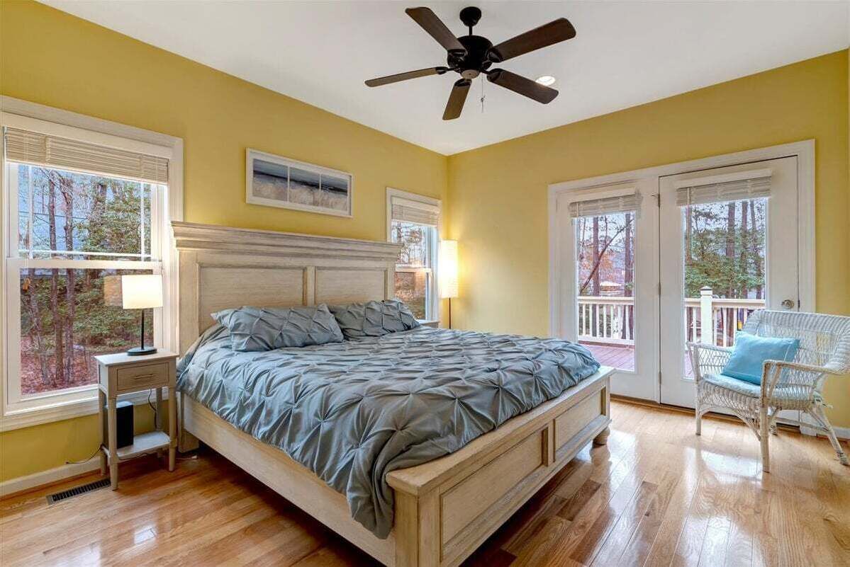A bedroom with a bed, a ceiling fan, a nightstand, a chair, and a view of the outdoors.