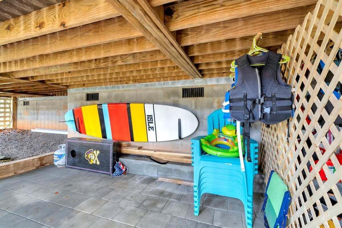 Un'area esterna riparata con una tavola da surf appoggiata al muro, una sedia blu e un giubbotto di salvataggio nero su un supporto.