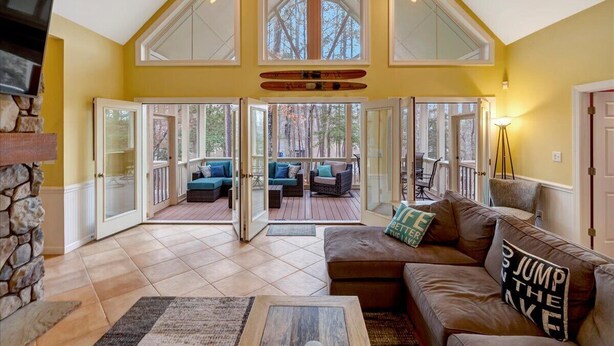 A spacious living area with a high ceiling, large windows, and a cozy seating area. - Water You Wating For? | Waterfront Fun & Relaxation (Boydton)
