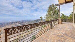 A stone-paved balcony with a decorative metal railing overlooking a mountainous landscape.