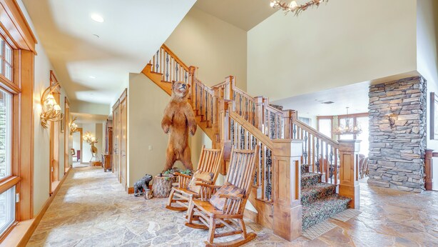A spacious hallway with a wooden staircase, a bear statue, and a stone fireplace.