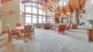 A spacious living room with a high ceiling, large windows, and a stone fireplace.