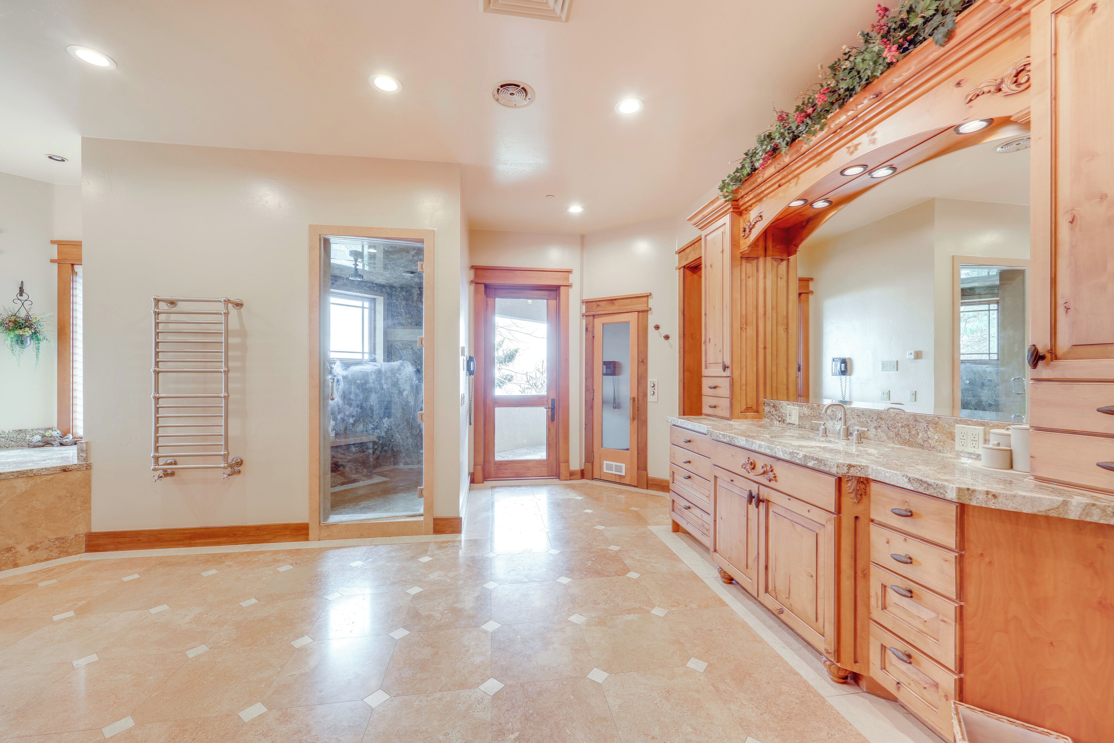 A spacious bathroom with a large mirror, wooden cabinetry, and a tiled floor.