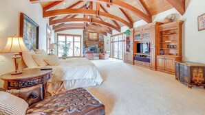 A spacious living room with a high wooden ceiling, a fireplace, and a large television.