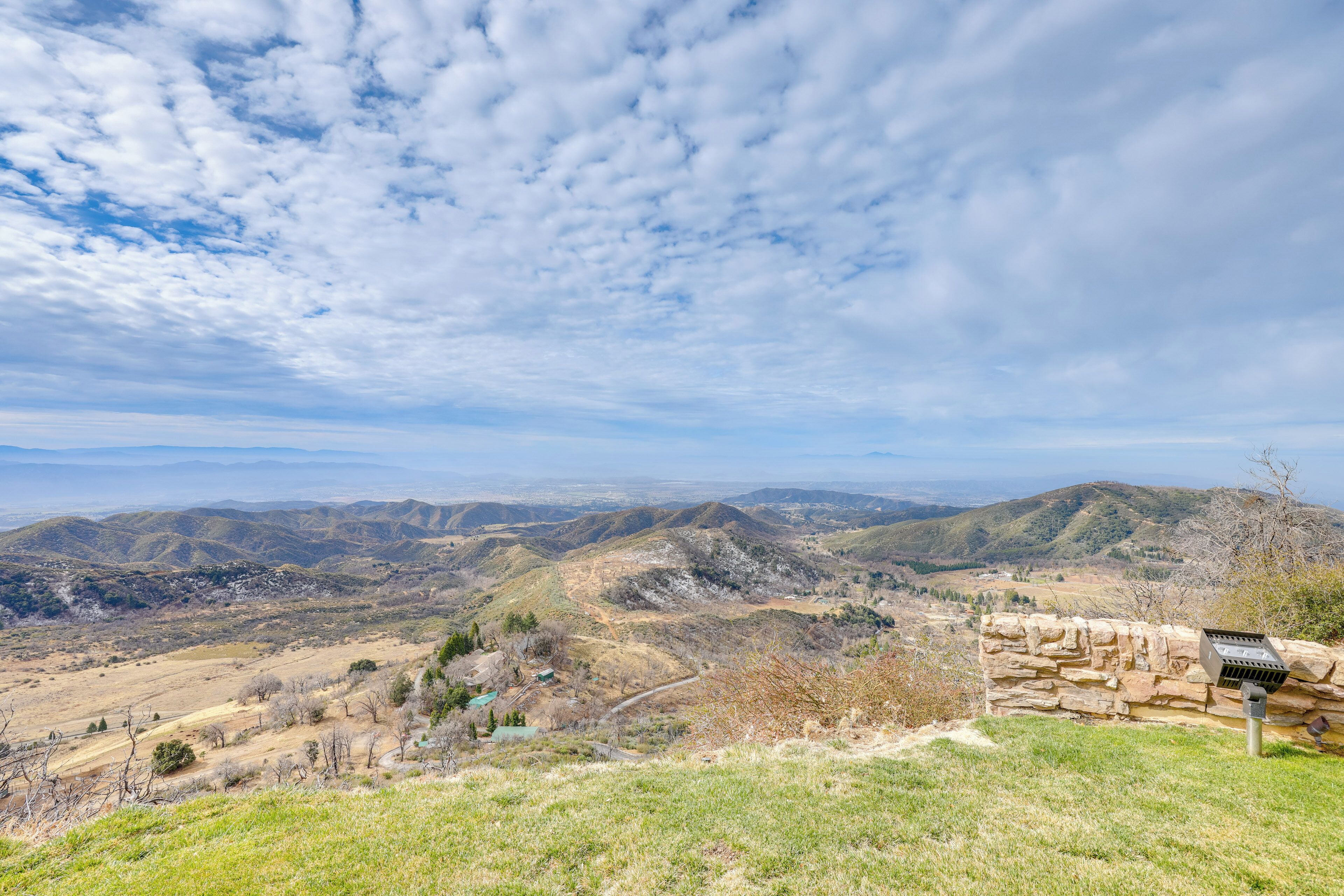 Un paisaje montañoso con un muro de piedra y una estructura metálica en primer plano, probablemente un buzón.