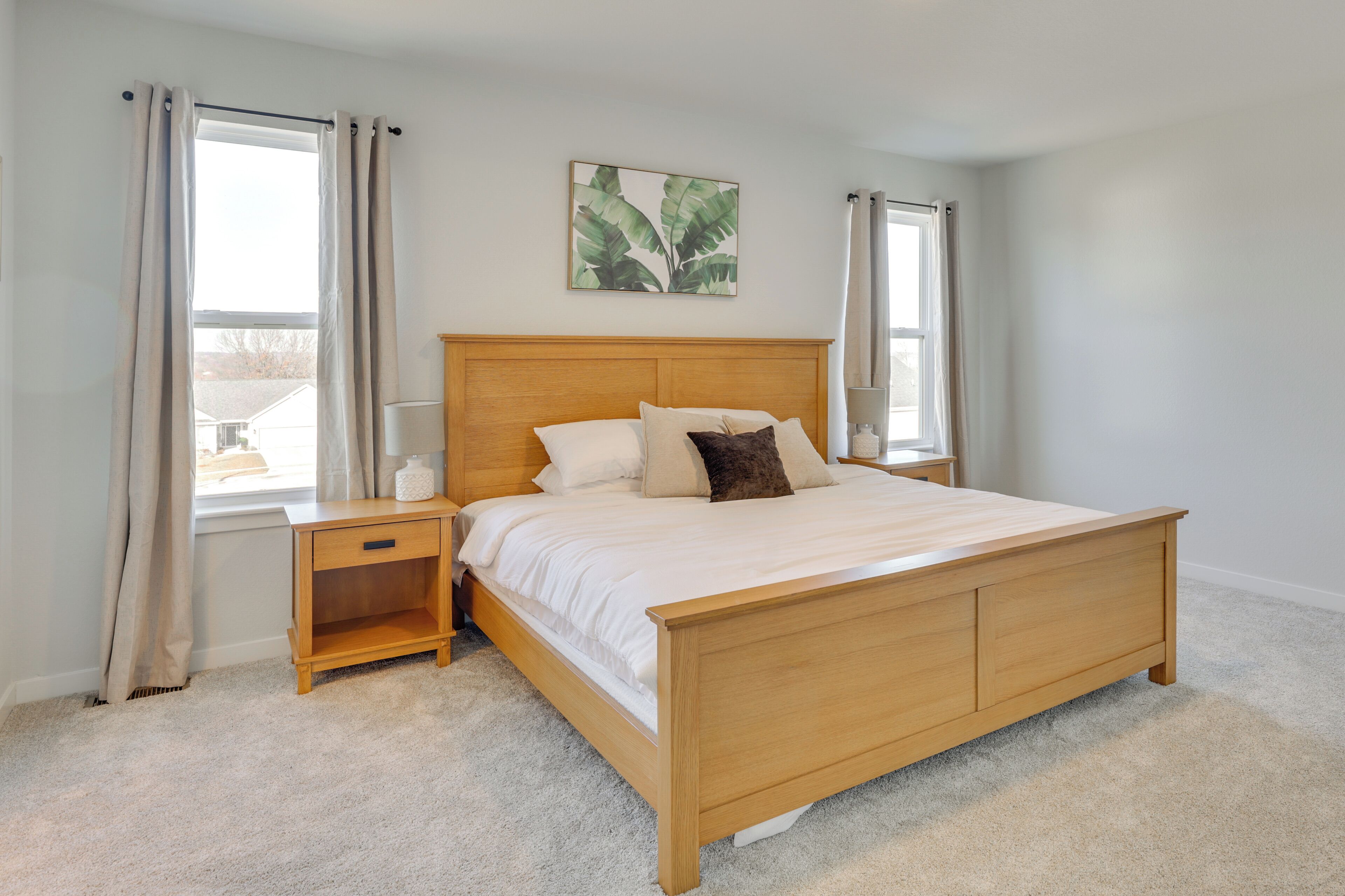 A bedroom with a wooden bed, two bedside tables, a nightstand, a window with curtains, and a wall-mounted plant.