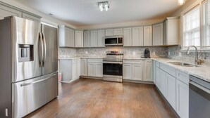 A modern kitchen with stainless steel appliances, white cabinetry, and a tiled backsplash. - Updated & Charming! Home Near Douthat State Park (Clifton Forge)