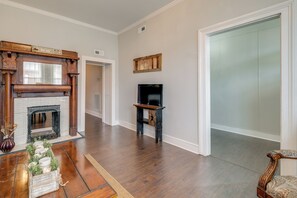 Un salon spacieux doté d’un parquet, d’une cheminée, d’un téléviseur posé sur un meuble et d’une porte donnant sur une autre pièce.