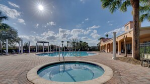 Zona de piscina con dos piscinas, rodeada por un paseo de ladrillos y palmeras.