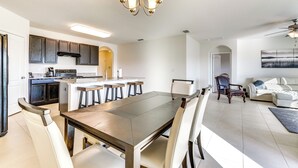 Una cocina moderna con armarios de madera oscura, una isla central con taburetes y un área de comedor con una mesa grande y sillas.