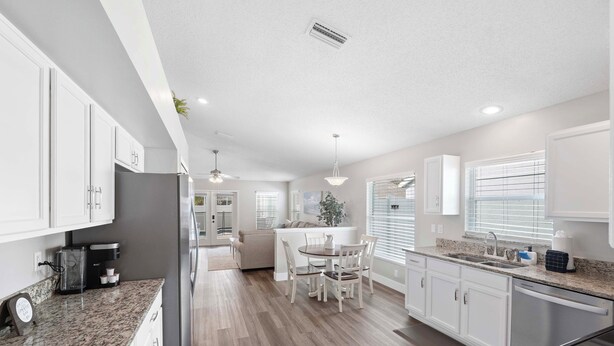 A modern kitchen with white cabinets, granite countertops, and a dining area with a table and chairs. - Saltwater Pool & Spa at Home in Bradenton (Bradenton)