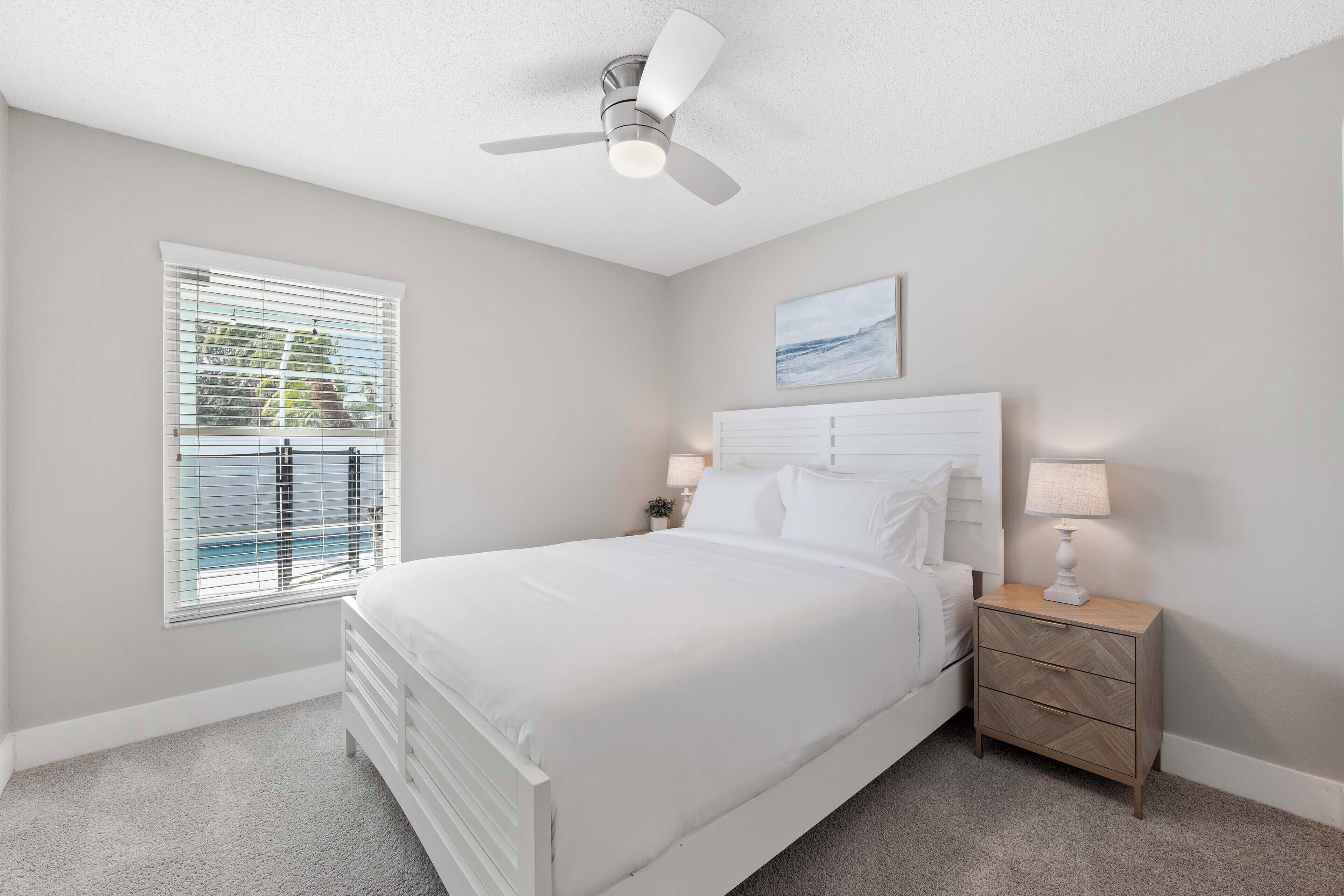 A bedroom with a bed, nightstand, lamp, and ceiling fan.