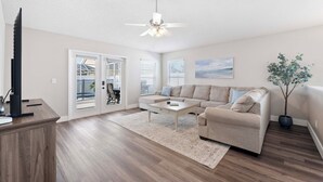 A spacious living room with a large sofa, a coffee table, a TV, and a ceiling fan. - Saltwater Pool & Spa at Home in Bradenton (Bradenton)