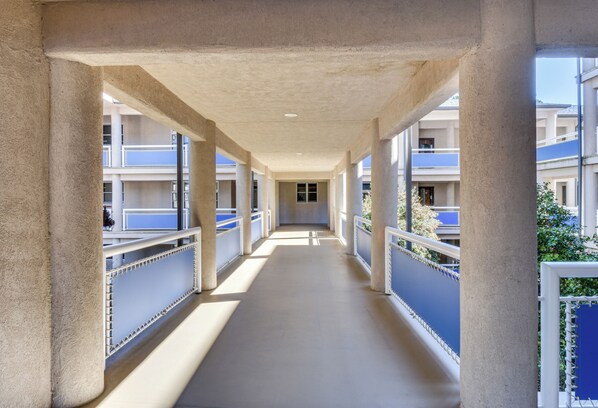 Un pasillo con columnas, barandillas y vistas a un edificio con balcones.