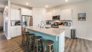 A modern kitchen with white cabinets, a central island with stools, stainless appliances, and a tiled backsplash. - 6 Mi to Bethany Beach: Family Home w/ Pool Access! (Millville)
