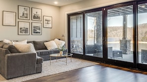 A living room with a gray sectional sofa, a coffee table, and a large sliding glass door leading to an outdoor patio. - Lakefront Gem: Dock & Hot Tub in Jacksboro (Jacksboro)