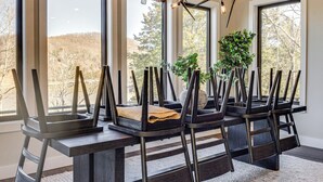 A dining area with a long table, multiple chairs, and large windows offering a view of trees and hills. - Lakefront Gem: Dock & Hot Tub in Jacksboro (Jacksboro)