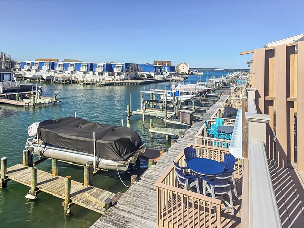 A marina with docked boats, a covered boat, and a wooden deck with blue chairs and tables.