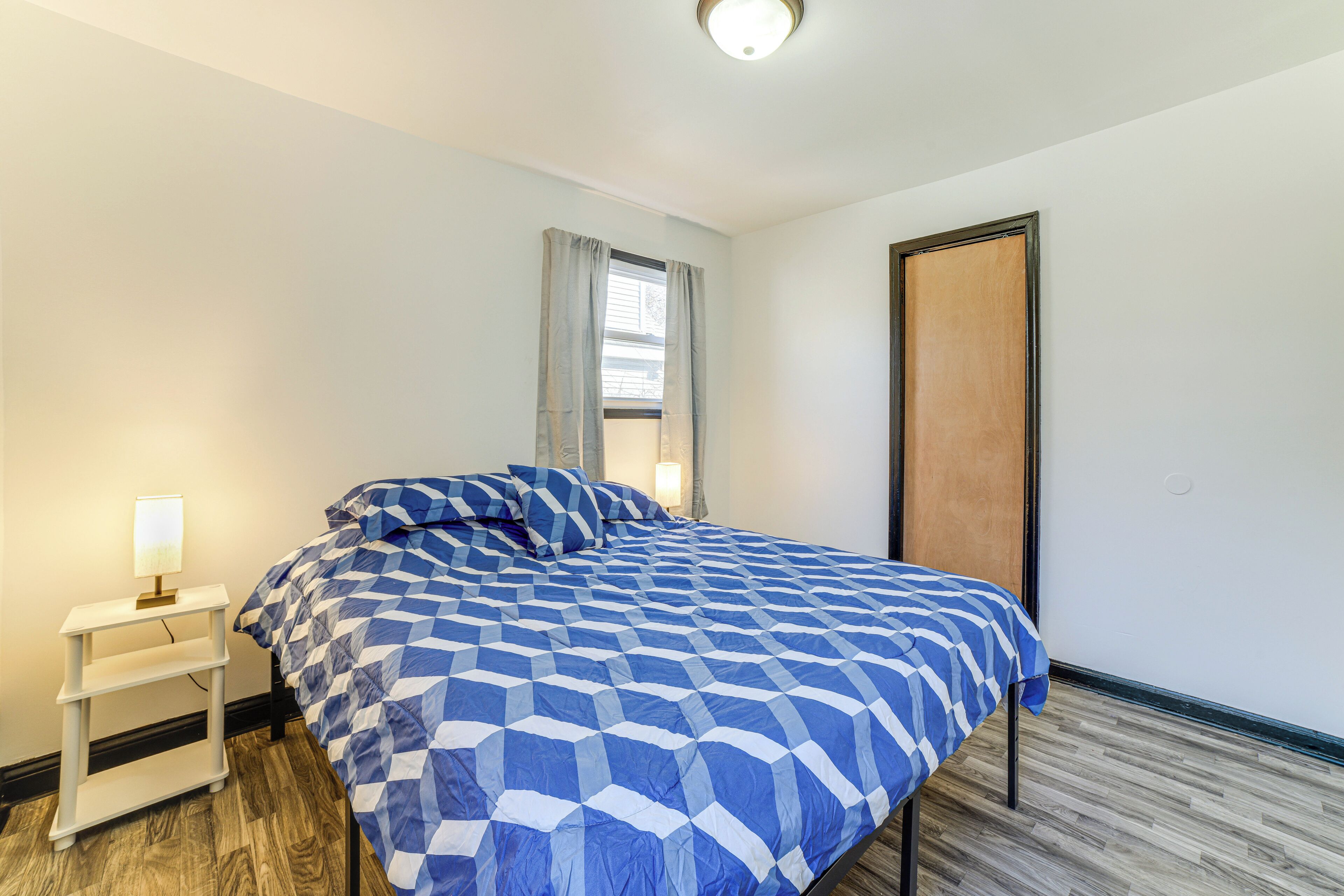 Une chambre à coucher avec un lit, une table de chevet, une fenêtre avec des rideaux et une porte.