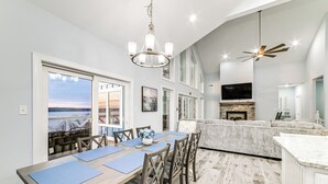 A modern dining area with a wooden table and chairs, a chandelier, and a view of the outdoors.
