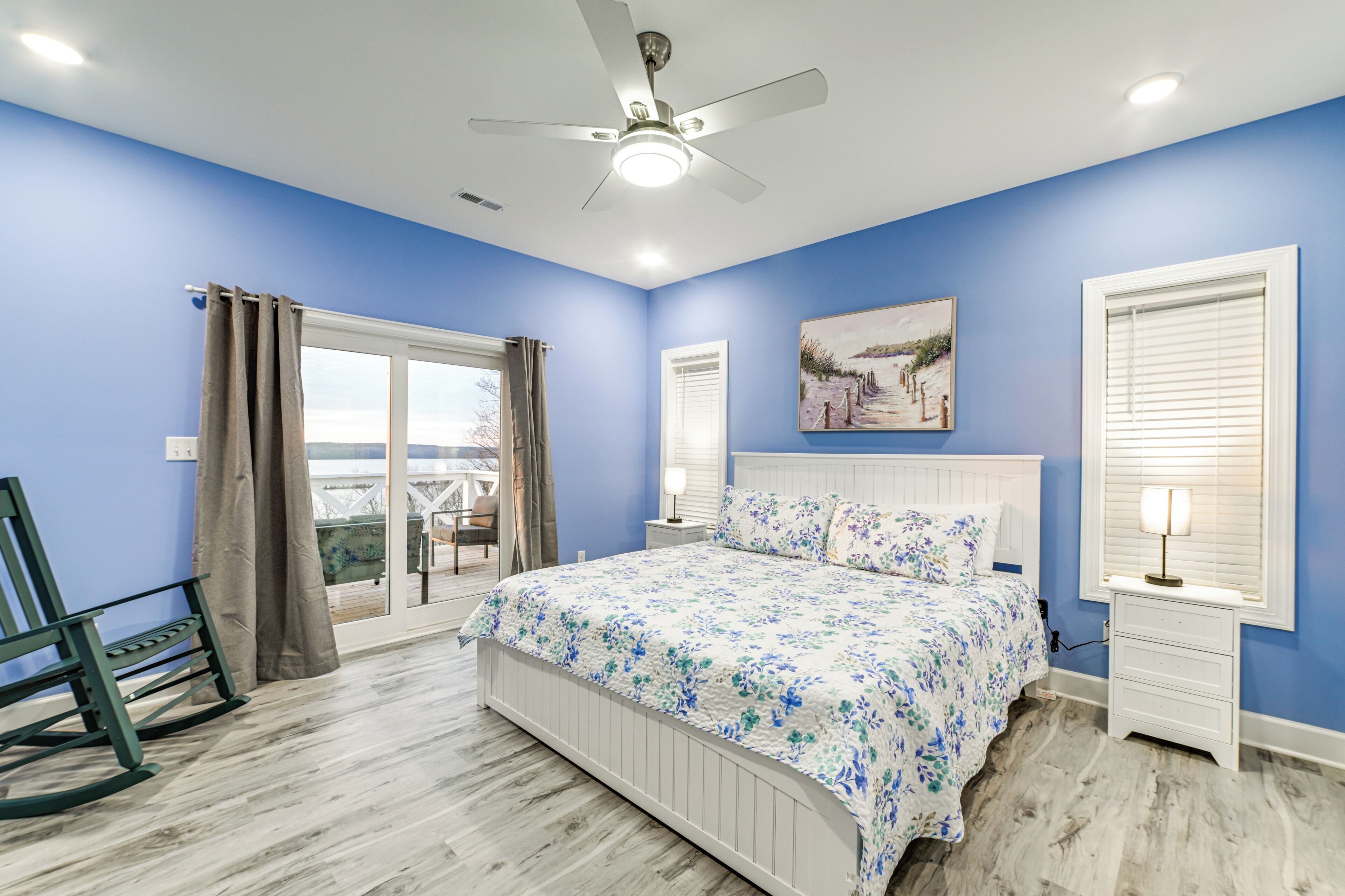 A bedroom with a bed, a nightstand, a chair, a ceiling fan, and a window with curtains.
