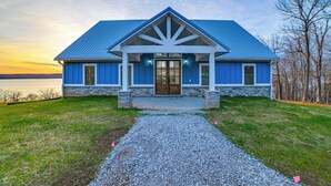 A house with a blue roof, stone foundation, and a gravel driveway leading to the front door.