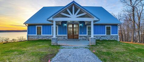 A house with a blue roof, stone foundation, and a gravel driveway leading to the front door.