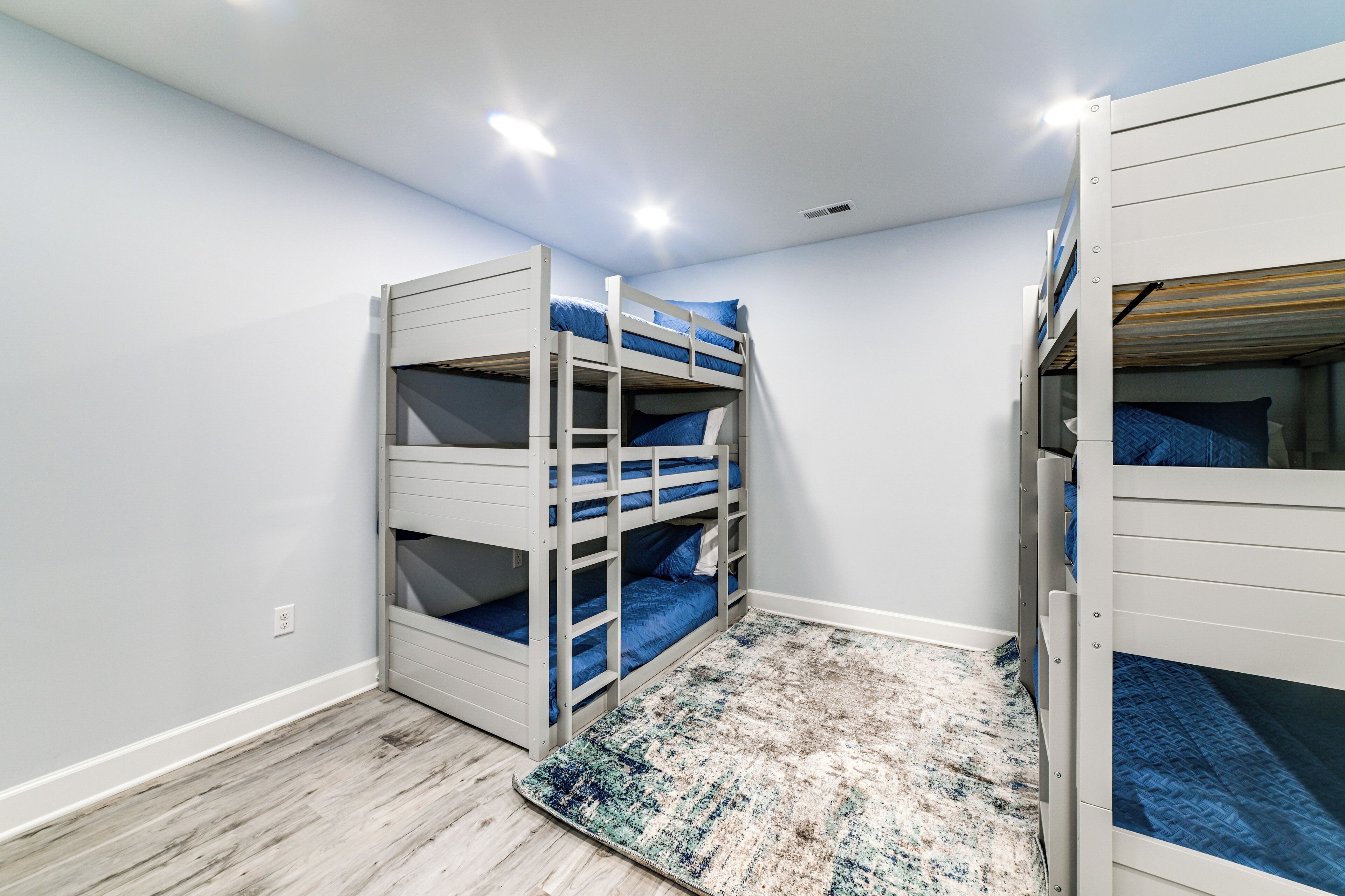 A room with bunk beds, a patterned rug, and a light-colored wooden floor.