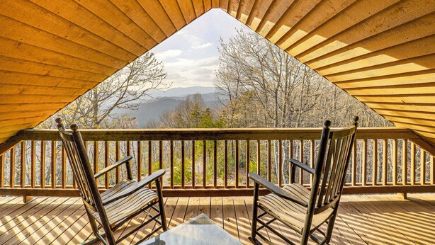 Un dormitorio en el ático con techo de madera y un balcón de madera con vistas a árboles y montañas.