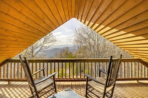 Een zolderkamer met houten plafond, een houten balkon met uitzicht op bomen en bergen.