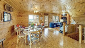 Interior de una cabaña de madera con comedor, sala de estar y escalera.