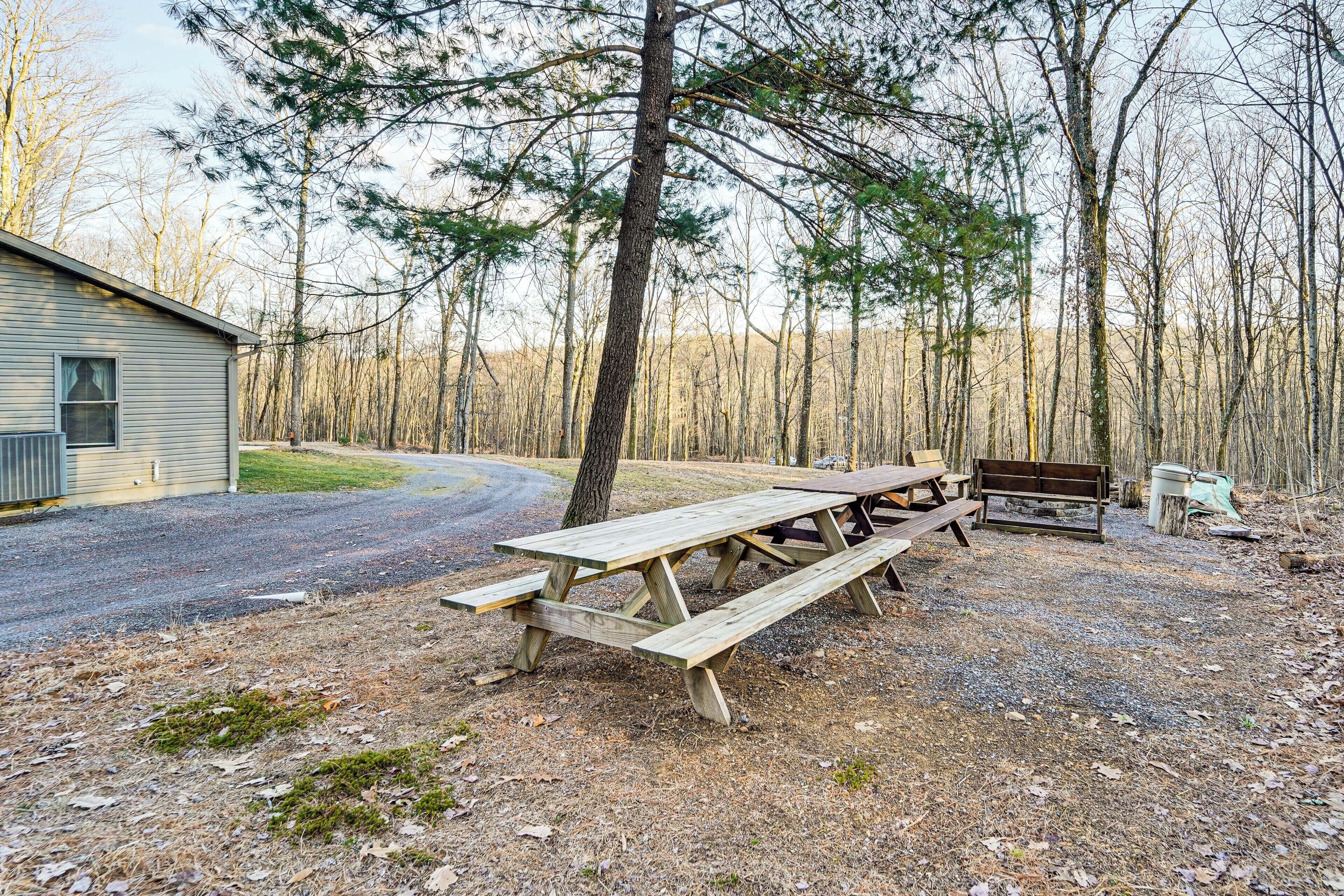 A picnic table and bench in a wooded area with a building in the background.