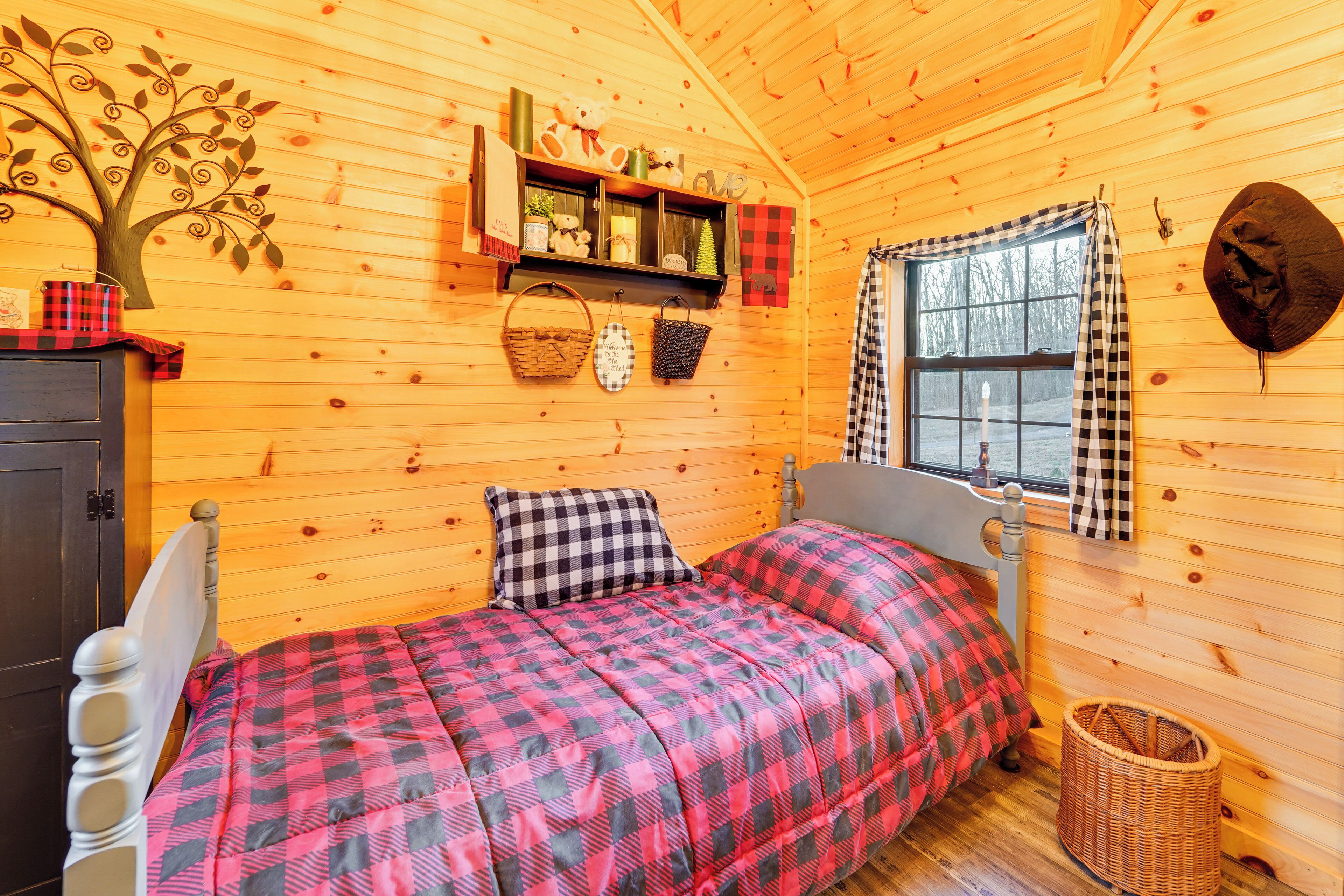 Une pièce chaleureuse, aménagée dans une cabane en bois, comprenant un lit, une commode, une fenêtre avec des rideaux et une étagère fixée au mur, sur laquelle sont disposés divers objets.
