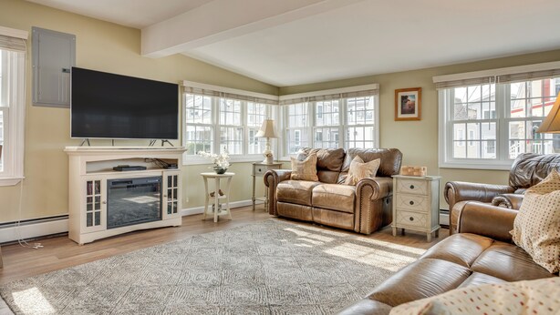 Een ruime woonkamer met een grote flatscreen televisie, leren banken, een open haard en grote ramen.