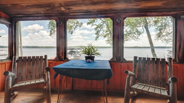 A wooden cabin with a table and two chairs, a potted plant, and a view of a lake and boats. - South Twin Lake Cabin w/ Seasonal Dock & Slip! (Conover)