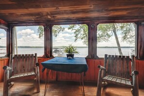A wooden cabin with a table and two chairs, a potted plant, and a view of a lake and boats. - South Twin Lake Cabin w/ Seasonal Dock & Slip! (Conover)