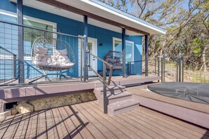 A wooden deck with a swing chair and a cushioned chair, a trampoline, and a blue building with large windows. - Close to Canyon Lake: Cabin - Boat Ramp & Hot Tub (Canyon Lake)