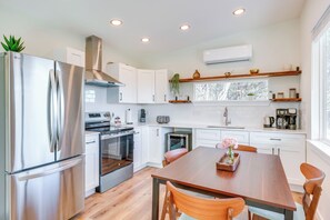 A modern kitchen with white cabinets, stainless steel appliances, a wooden dining table, and a window with a view of trees. - Close to Canyon Lake: Cabin - Boat Ramp & Hot Tub (Canyon Lake)
