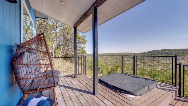 Eine Holzterrasse mit einem Korbstuhl und einer Matratze mit Blick auf eine hügelige Landschaft.