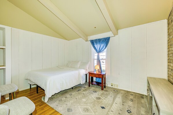 A bedroom with a bed, a small table, a chair, and a window with a curtain. - 9 Mi to Dtwn: Spacious Retreat in Corpus Christi! (Corpus Christi)
