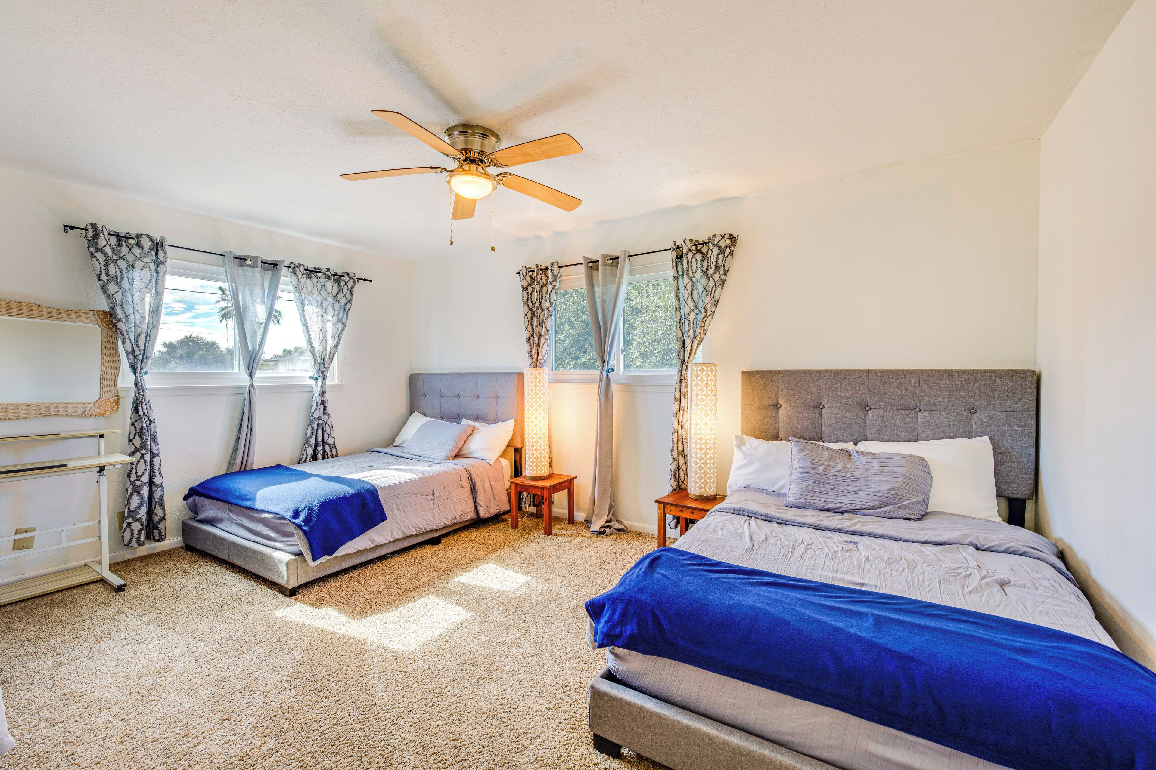 Un dormitorio con dos camas, un ventilador de techo y una ventana con cortinas.