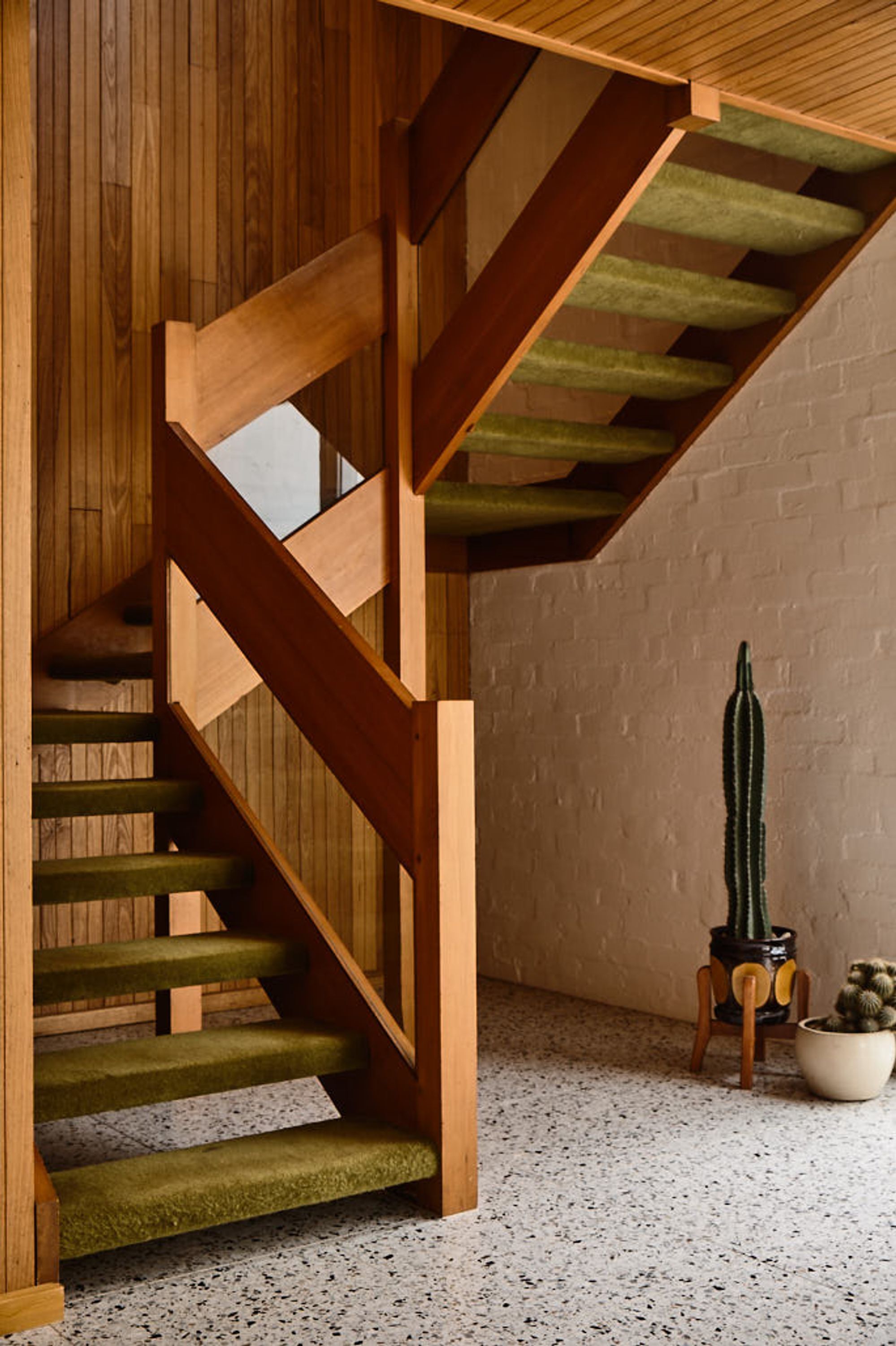 A wooden staircase with a unique design, a cactus plant, and a small table with a pot.