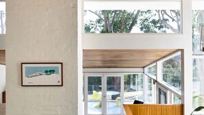Una sala de estar moderna con chimenea, un comedor con una mesa redonda y sillas, y grandes ventanas que ofrecen vistas al exterior.