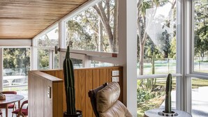 Una habitación moderna con ventanas amplias, un cactus, una silla de descanso y una mesita.