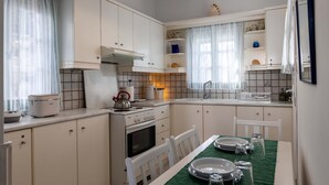 A compact kitchen with white cabinets, a stove, and a dining table set for four. - Naoussa Breeze Residence (Paros)