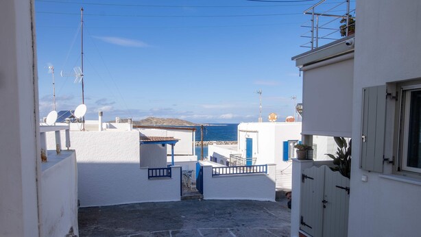 A narrow street with white buildings, a gate, and a view of the sea. - Naoussa Breeze Residence (Paros)