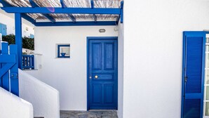 A white building with a blue door and blue shutters, stone steps, and a small window. - Naoussa Breeze Residence (Paros)
