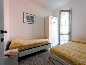 A small, clean room with two single beds, a wardrobe, a framed picture on the wall, and a window with curtains. - Relaxing Townhouse With Pool Access in Bibione (San Michele al Tagliamento)